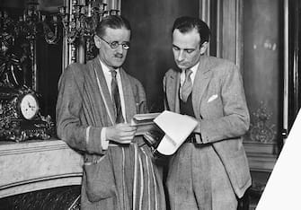 Author James Joyce looks at a set of papers with another man.