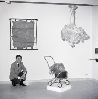 (Original Caption) 11/29/1963-Rome, Italy- The art of wrapping, called "Empaquetage" by artist Christo, features all shapes and sizes creatively covered..."The purpose of which is to reveal the loving form of mystery," he says. The 28-year-old, Bulgarian-born artist creates with such wrappings as cellophane, canvas or blankets and ties the objects with any string available at the time. Here, Christo is seen surrounded by his "Objects D'Art" which he displayed at the La Salita Gallery in Rome, Italy.