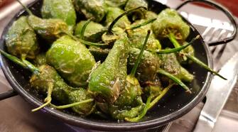 BARCELONA, SPAIN - OCTOBER 6: The Spanish delicacy of fried PadrÃ³n peppers (pimientos del padron) are served to customers seated at the counter at Bar Quiosco Moderno, a popular seafood and tapas bar in Mercat de Sant Josep, better known as La Boqueria, on October 6, 2018 in Barcelona, Spain. The city, which is known for its art, architecture and gastronomic diversity, hosts over 4.5 million tourists annually. It is also the center of the Catalan independence movement and has seen violent protests and mass demonstrations in the drive for Catalan independence from Spain. (Photo by David Silverman/Getty Images)