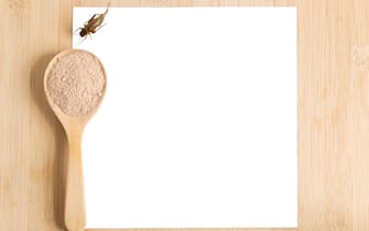 Cricket powder insect for eating and cooking food in wooden spoon with white paper mockup on wood background it is good source of protein edible for future food. Entomophagy concept. Top view.