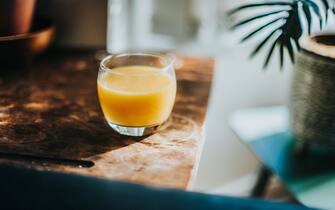 A single glass of fresh orange juice, sitting on top of a dark wood table in morning sunlight.