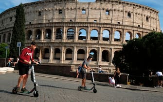 People ride electric scooters of Italian-American intra-urban transportation company Helbiz, on May 28, 2020 past the Colosseum monument in Rome as the country eases its lockdown aimed at curbing the spread of the COVID-19 infection, caused by the novel coronavirus. (Photo by Andreas SOLARO / AFP) (Photo by ANDREAS SOLARO/AFP via Getty Images)