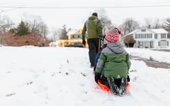 Rear view of father pulling children through the snow on  orange sled