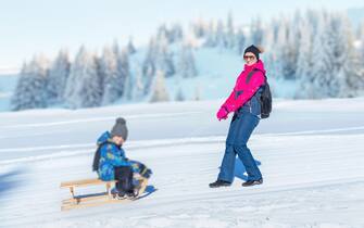 Mother dragging the snow sled with boy. Mountain in background. Concept od keep children healthy during the winter