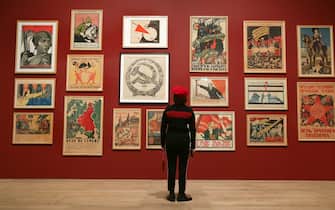 A visitor poses in front of a mural with various posters including:  artist Adolf Strakhov's 'Emancipated Woman: Build socialism!' c. 1926 (top-L) and artist Valentin Shcherbakov's 'A Spectre is Haunting Europe, the Spectre of Communism' c. 1924, during the 'Red Star over Russia: A revolution in Visual Culture 1905-55' exhibition at the Tate Modern in London on November 7, 2017. / AFP PHOTO / Daniel LEAL-OLIVAS / RESTRICTED TO EDITORIAL USE - MANDATORY MENTION OF THE ARTIST UPON PUBLICATION - TO ILLUSTRATE THE EVENT AS SPECIFIED IN THE CAPTION        (Photo credit should read DANIEL LEAL-OLIVAS/AFP via Getty Images)