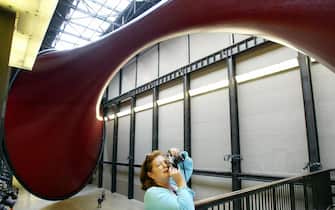 A visitor photographs "Marsyas", a gigantic sculpture created by Anish Kapoor, at The Tate Modern gallery in London 09 October 2002. The installation measures 155 metres long, 23m wide and 35m high and consists of three steel rings joined by a single span of PVC membrane. The title Marsyas refers to the satyr in Greek mythology, who was flayed by the god Apollo. The exhibit is the first time one piece has filled the entire Turbine Gallery.  AFP PHOTO ADRIAN DENNIS (Photo credit should read ADRIAN DENNIS/AFP via Getty Images)
