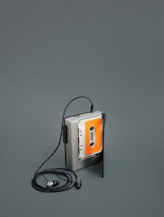 Gray portable analog audio cassette player with wired black earbuds and white cassette tape with orange label inside. Gray background. Vintage and retro style concept.