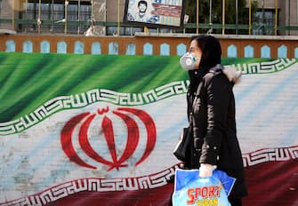 An Iranian woman wearing a mask walks past a mural displaying her national flag in Tehran on March 4, 2020. - Iran has scrambled to halt the rapid spread of the COVID-19 virus, shutting schools and universities, suspending major cultural and sporting events, and cutting back on work hours. (Photo by ATTA KENARE / AFP) (Photo by ATTA KENARE/AFP via Getty Images)