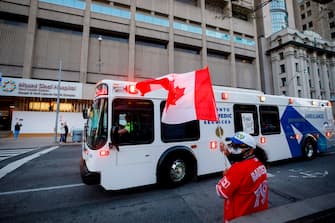 A man waves a Canadian flag as first responders parade down hospital row in Toronto, Ontario, Canada, in a salute to healthcare workers on April 19, 2020, amid the novel coronavirus pandemic. - The worldwide death toll from the novel coronavirus pandemic rose to 164,016 on April 19, according to a tally from official sources compiled by AFP at 1900 GMT. (Photo by Cole BURSTON / AFP) (Photo by COLE BURSTON/AFP via Getty Images)