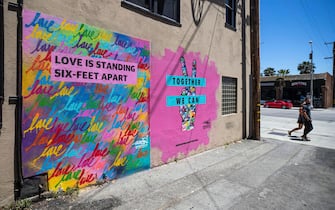 epa08406397 A couple walks past a mural by Mr. Rojas reading 'Love is Standing Six-Feet Apart' and 'Together We can' amid the coronavirus pandemic in Santa Monica, California, USA, 06 May 2020.  EPA/ETIENNE LAURENT