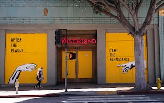 epa08406399 A couple wearing face masks walks the boarded clothing shop 'Wasteland' displaying a mural by Corie Mattie that reads 'After the Plague Came the Renaissance' amid the coronavirus pandemic in Santa Monica, California, USA, 06 May 2020.  EPA/ETIENNE LAURENT