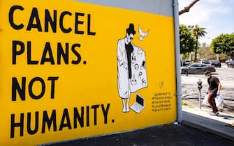 epa08406401 A man carrying groceries and wearing a face mask walks past a mural by Corie Mattie that reads 'Cancel Plans Not Humanity' amid the coronavirus pandemic in Los Angeles, California, USA, 06 May 2020.  EPA/ETIENNE LAURENT