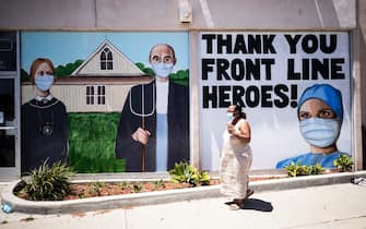 epa08406398 A woman wearing a face mask walks past the boarded windows of Silvio's Photoworks displaying an interpretation of 'American Gothic' with the characters wearing face masks and the words 'Thank You Front Line Heroes' over the drawing of a medical worker amid the coronavirus pandemic in Torrance, South of Los Angeles, California, USA, 06 May 2020.  EPA/ETIENNE LAURENT