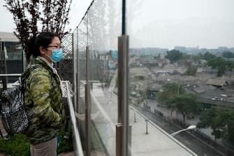 BEIJING, CHINA - MAY 08:  A Chinese woman wears a protective mask as she looks on at a restaurant balcony on May 8, 2020 in Beijing, China. Life in Beijing is slowly returning to normal following a city-wide lockdown on January 25 to contain the coronavirus (COVID-19) outbreak. (Photo by Lintao Zhang/Getty Images)