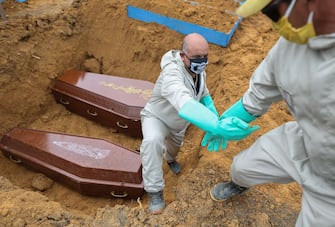 Brazilian Ulisses Xavier, 52, who has worked for 16 years at Nossa Senhora cemetery in Manaus, Brazil, is helped out from a grave by a co-worker during their shift on May 8, 2020, amid the new coronavirus pandemic. - Xavier works 12 hours a day and supplements his income by making wooden crosses for graves. The cemetery has seen a surge in the number of new graves after the outbreak of COVID-19. (Photo by MICHAEL DANTAS / AFP) (Photo by MICHAEL DANTAS/AFP via Getty Images)