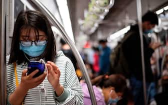 A passenger wearing a facemask uses her mobile phones at the subway in Beijing on May 12, 2020. (Photo by Noel CELIS / AFP) (Photo by NOEL CELIS/AFP via Getty Images)