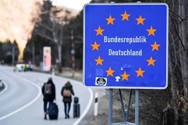 epa08418763 (FILE) - Two people witht their trolley bags walk past a road sign at the border crossing between Germany and Austria in Scharnitz, Germany, 16 March 2020 (reissued 13 May 2020). Media reports state on 13 May 2020 that Germany is planning to partially ease border controls as early as 16 May 2020, following a decision of the Cabinet. At the same time, Austria is planning to reopen the border with Germany as early as 15 June, media added.  EPA/PHILIPP GUELLAND *** Local Caption *** 55955852