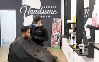 A barber wearing a face mask cuts a customer's hair in Wellington on May 14, 2020. - New Zealand will phase out its coronavirus lockdown over the next 10 days after successfully containing the virus, although some restrictions will remain, Prime Minister Jacinda Ardern announced on May 11. Ardern said that from May 14 shopping malls, restaurants, cinemas and playgrounds will reopen -- with the country moving to Level Two on its four-tier system. (Photo by Marty MELVILLE / AFP) (Photo by MARTY MELVILLE/AFP via Getty Images)