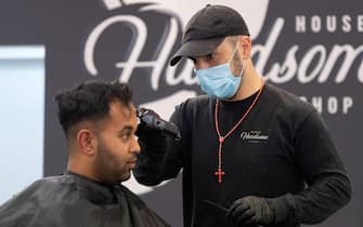 A barber wearing a face mask cuts a customer's hair in Wellington on May 14, 2020. - New Zealand will phase out its coronavirus lockdown over the next 10 days after successfully containing the virus, although some restrictions will remain, Prime Minister Jacinda Ardern announced on May 11. Ardern said that from May 14 shopping malls, restaurants, cinemas and playgrounds will reopen -- with the country moving to Level Two on its four-tier system. (Photo by Marty MELVILLE / AFP) (Photo by MARTY MELVILLE/AFP via Getty Images)