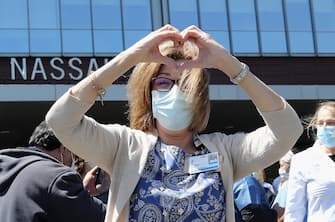 1224662606 OCEANSIDE, NEW YORK - MAY 13: Frontline hospital worker Suzanne Mayer of Mount Sinai South Nassau Hospital poses for a photo as first responders including the Nassau County Police Department's 'Pipes & Drums' salute them on May 13, 2020 in Oceanside, New York. (Photo by Bruce Bennett/Getty Images)
