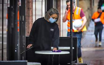 SYDNEY, AUSTRALIA - MAY 15: A worker wearing a face mask cleans a table for customers on May 15, 2020 in Sydney, Australia. Restrictions put in place in response to the COVID-19 outbreak have been eased in New South Wales as of today, with social distancing measures relaxed in response to Australia's declining number of confirmed coronavirus cases. From Friday 15 May cafes and restaurants along with pub and club dining areas are allowed to reopen for up to 10 patrons at a time. Outdoor gatherings of up to 10 people are now also permitted, while outdoor gyms, playgrounds, swimming pools can also open. Up to 10 guests can attend a wedding while 20 mourners are permitted for an indoor funeral, or 30 can attend if the service is outdoors. Religious gatherings and places of worship can have 10 worshipers at one time, while people are permitted to have up to five visitors in their homes at any one time. (Photo by David Gray/Getty Images)