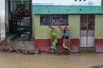 TOPSHOT - Residents walk along a house on a flooded street heading to a shelter ahead of the expected landfall of cyclone Amphan, in Dacope of Khulna district on May 20, 2020. - Several million people were taking shelter and praying for the best on Wednesday as the Bay of Bengal's fiercest cyclone in decades roared towards Bangladesh and eastern India, with forecasts of a potentially devastating and deadly storm surge. Authorities have scrambled to evacuate low lying areas in the path of Amphan, which is only the second "super cyclone" to form in the northeastern Indian Ocean since records began. (Photo by Munir uz Zaman / AFP) (Photo by MUNIR UZ ZAMAN/AFP via Getty Images)