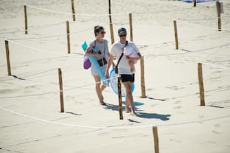 A man and woman walk past roped off distancing zones marked out by the municipality at 'Couchant or Sunset beach' in La Grande Motte, southern France, on May 21, 2020, as the nation eases lockdown measures taken to curb the spread of the COVID-19 pandemic, caused by the novel coronavirus. - The local municipality dubbed this set up 'organized beaches', the first in France to implement separated zones for beach goers in order to respect social distancing. (Photo by CLEMENT MAHOUDEAU / AFP)