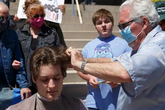 LANSING, MI - MAY 20: Owosso barber, Karl Manke, gives a free haircut to Parker Shonts, of Lake Orion, on the steps of the state Capitol during Operation Haircut on May 20, 2020 in Lansing, Michigan. The event was a protest planned by the Michigan Conservative Coalition in response to an Owosso barber, Karl Manke, whose business license was taken away after he violated the stay-at-home order by reopening. The protest is part of a growing national movement against stay-at-home orders that are designed to help slow the spread of the coronavirus (COVID-19). (Photo by Elaine Cromie/Getty Images)