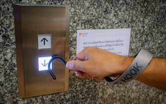 This photo illustration shows a hook tool on a strap, intended to enable hands free interactions with objects amid concern over the spread of the COVID-19 coronavirus, as it is used to press an elevator button in an office building in Bangkok on May 22, 2020. (Photo by Mladen ANTONOV / AFP) (Photo by MLADEN ANTONOV/AFP via Getty Images)
