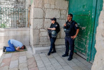 Israeli security forces look on as a Palestinian worshipper performs the last Friday prayer of the Muslim holy month of Ramadan, outside the closed al-Aqsa mosque compound in the Old City of Jerusalem, amid the novel coronavirus pandemic crisis, on May 22, 2020. (Photo by AHMAD GHARABLI / AFP) (Photo by AHMAD GHARABLI/AFP via Getty Images)