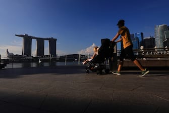 SINGAPORE - MAY 26:  A woman wearing protective mask pushes a stroller with the Marina Bay Sands, ArtScience museum and the central business district pictured in the background on May 26, 2020 in Singapore. Singapore is set to ease the partial lockdown measures against the coronavirus (COVID-19) pandemic after 1 June in three phases to resume activities safely after it sees a decline in the new infection cases in the community. Singapore's gross domestic product (GDP) is expected to shrink as much as 7 percent this year as the country battles the slump in global trade and travel amid the coronavirus pandemic, according to the government report in the local media today.  (Photo by Suhaimi Abdullah/Getty Images)