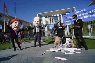 BERLIN, GERMANY - MAY 27: An activist dressed as German Chancellor Angela Merkel throws a paper airplane as another dressed as Finance Minister Olaf Scholz looks on during a small protest outside the Chancellery against the recent Lufthansa bailout on May 27, 2020 in Berlin, Germany. The German government announced Monday it will prop up German airline Lufthansa with a EUR 9 billion package that includes a 20% government stake in the company. The activists were protesting both against the fiscal and the environmental implications of the bailout.  (Photo by Sean Gallup/Getty Images)