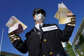 BERLIN, GERMANY - MAY 27: An activist dressed as an airline stewardess holds up oversized fake versions of Euro currency at a protest outside the Chancellery against the recent Lufthansa bailout during the coronavirus crisis on May 27, 2020 in Berlin, Germany. The German government announced Monday it will prop up German airline Lufthansa with a EUR 9 billion package that includes a 20% government stake in the company. The activists were protesting both against the fiscal and the environmental implications of the bailout.  (Photo by Sean Gallup/Getty Images)
