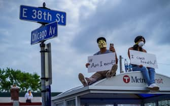 People hold signs and sit on a bus stop during a protest near where a Minneapolis Police Department officer allegedly killed George Floyd, on May 26, 2020 in Minneapolis, Minnesota. - A video of a handcuffed black man dying while a Minneapolis officer knelt on his neck for more than five minutes sparked a fresh furor in the US over police treatment of African Americans Tuesday. Minneapolis Mayor Jacob Frey fired four police officers following the death in custody of George Floyd on Monday as the suspect was pressed shirtless onto a Minneapolis street, one officer's knee on his neck. (Photo by kerem yucel / AFP) (Photo by KEREM YUCEL/AFP via Getty Images)