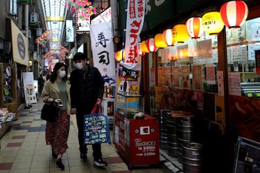 OSAKA, JAPAN - MARCH 29: A couple wearing face masks walk through an empty shopping district usually busy with tourists and shoppers on March 29, 2020 in Osaka, Japan. Japanâ  s two most populated cities, Tokyo and Osaka, urged residents to refrain from non-essential travel this weekend, to contain the spread of the coronavirus. Travelers and shoppers have disappeared from inner city and sightseeing spots in response to the request and avoiding the spread of coronavirus (COVID-19) infections. On Saturday, Japan has reported 200 coronavirus infection cases in a single day for the first time. (Photo by Buddhika Weerasinghe/Getty Images)