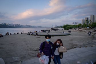 In a photo taken on May 24, 2020, people wearing face masks amid concerns of the COVID-19 novel coronavirus walk through a park before the Han river in Seoul. (Photo by Ed JONES / AFP) (Photo by ED JONES/AFP via Getty Images)
