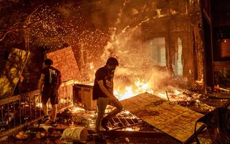 Protesters walk past burning debris outside the Third Police Precinct on May 28, 2020 in Minneapolis, Minnesota, during a protest over the death of George Floyd, an unarmed black man, who died after a police officer kneeled on his neck for several minutes. - A police precinct in Minnesota went up in flames late on May 28 in a third day of demonstrations as the so-called Twin Cities of Minneapolis and St. Paul seethed over the shocking police killing of a handcuffed black man. The precinct, which police had abandoned, burned after a group of protesters pushed through barriers around the building, breaking windows and chanting slogans. A much larger crowd demonstrated as the building went up in flames. (Photo by Kerem Yucel / AFP) (Photo by KEREM YUCEL/AFP via Getty Images)