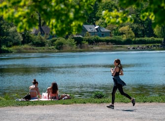 A woman jogs past sunbathers next to a canal at Djurgarden in Stockholm, on May 26, 2020, as temperatures reached 20 degrees Celsius. (Photo by Anders WIKLUND / TT News Agency / AFP) / Sweden OUT (Photo by ANDERS WIKLUND/TT News Agency/AFP via Getty Images)