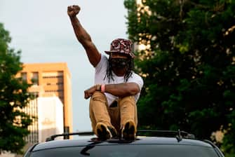 A demonstrator raises his fist while riding on top of a vehicle in Denver, Colorado on May 31, 2020, while protesting the death of George Floyd, an unarmed black man who died while while being arrested and pinned to the ground by the knee of a Minneapolis police officer. - Thousands of National Guard troops patrolled major US cities  after five consecutive nights of protests over racism and police brutality that boiled over into arson and looting, sending shock waves through the country. The death Monday of an unarmed black man, George Floyd, at the hands of police in Minneapolis ignited this latest wave of outrage in the US over law enforcement's repeated use of lethal force against African Americans -- this one like others before captured on cellphone video. (Photo by Jason Connolly / AFP) (Photo by JASON CONNOLLY/AFP via Getty Images)