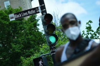1217780204 A woman is seen in front of a street sign for the newly proclaimed "Black Lives Matter Plaza" near the White House in Washington, DC, on June 5 2020. (Photo by MANDEL NGAN / AFP) (Photo by MANDEL NGAN/AFP via Getty Images)