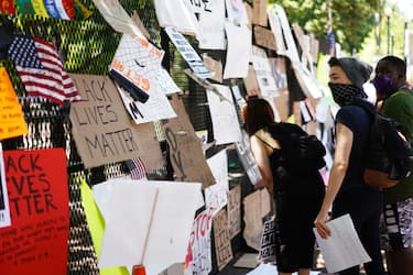 People look at posters and placards on the security fence on the north side of Lafayette Square, near the White House, in Washington, DC on June 8, 2020. - On May 25, 2020, Floyd, a 46-year-old black man suspected of passing a counterfeit $20 bill, died in Minneapolis after Derek Chauvin, a white police officer, pressed his knee to Floyd's neck for almost nine minutes. (Photo by MANDEL NGAN / AFP) (Photo by MANDEL NGAN/AFP via Getty Images)