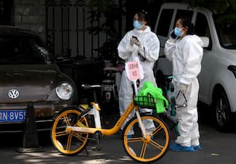 People wearing protective suits use their mobile phones near the Guangan Sport Center where swab tests for people that live or visited Xinfadi market is taking place in Beijing on June 15, 2020. - China locks down ten more Beijing neighbourhoods over virus cluster. (Photo by Noel Celis / AFP) (Photo by NOEL CELIS/AFP via Getty Images)
