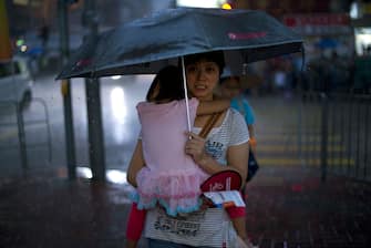A woman carries a child in torrential rain in Hong Kong on July 1, 2013 as thousands of protesters rally to mark the 16th anniversary of the establishment of the Hong Kong Special Administrative Region (HKSAR).   Tens of thousands of protesters marched through torrential rain in Hong Kong on July 1 chanting slogans against the city's Chief Executive Leung Chun-ying and demanding universal suffrage on the anniversary of the city's return to mainland rule.  AFP PHOTO / Alex OGLE        (Photo credit should read Alex Ogle/AFP via Getty Images)