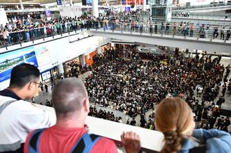 Tourists (foreground) watch from above as protesters rally against a controversial extradition bill in the arrivals hall of the international airport in Hong Kong on July 26, 2019. - Hundreds of protesters, including flight attendants, held a rally in the airport's arrival hall on July 26 in a bid to "educate" visitors about the unprecedented demonstrations recently taking place in the international finance hub. (Photo by Anthony WALLACE / AFP)        (Photo credit should read ANTHONY WALLACE/AFP via Getty Images)