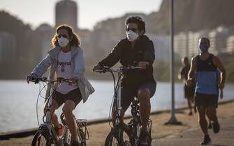 RIO DE JANEIRO, BRAZIL - JUNE 17: Cyclists wearing face masks ride by the Rodrigo de Freitas Lagoon amidst the coronavirus (COVID-19) pandemic on June 17, 2020 in Rio de Janeiro, Brazil. The city of Rio de Janeiro started today the second phase of the quarantine flexibilization. The decree determines the return of 100% of the bus fleet and some commercial establishments following distance rules such as reduced opening hours, restricting the flow of people and maintaining hygiene standards. (Photo by Andre Coelho/Getty Images)