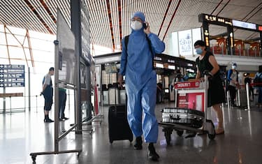 A man wearing a protective suit uses his phone at Beijing's international airport on June 17, 2020. - Beijing's airports cancelled more than 1,200 flights and schools in the Chinese capital were closed again on June 17 as authorities rushed to contain a new coronavirus outbreak linked to a wholesale food market. (Photo by STR / AFP) (Photo by STR/AFP via Getty Images)