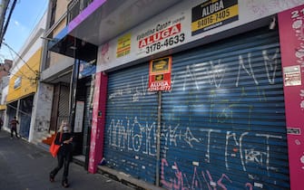 A woman walks past an empty store to rent in a comercial area of Sao Paulo, Brazil, on June 17, 2020. - Sao Paulo is resuming its economic activity, but in some streets of Brazil's largest metropolis a succession of low iron curtains is evidence of the impact of the coronavirus: merchants have closed down. (Photo by NELSON ALMEIDA / AFP) (Photo by NELSON ALMEIDA/AFP via Getty Images)