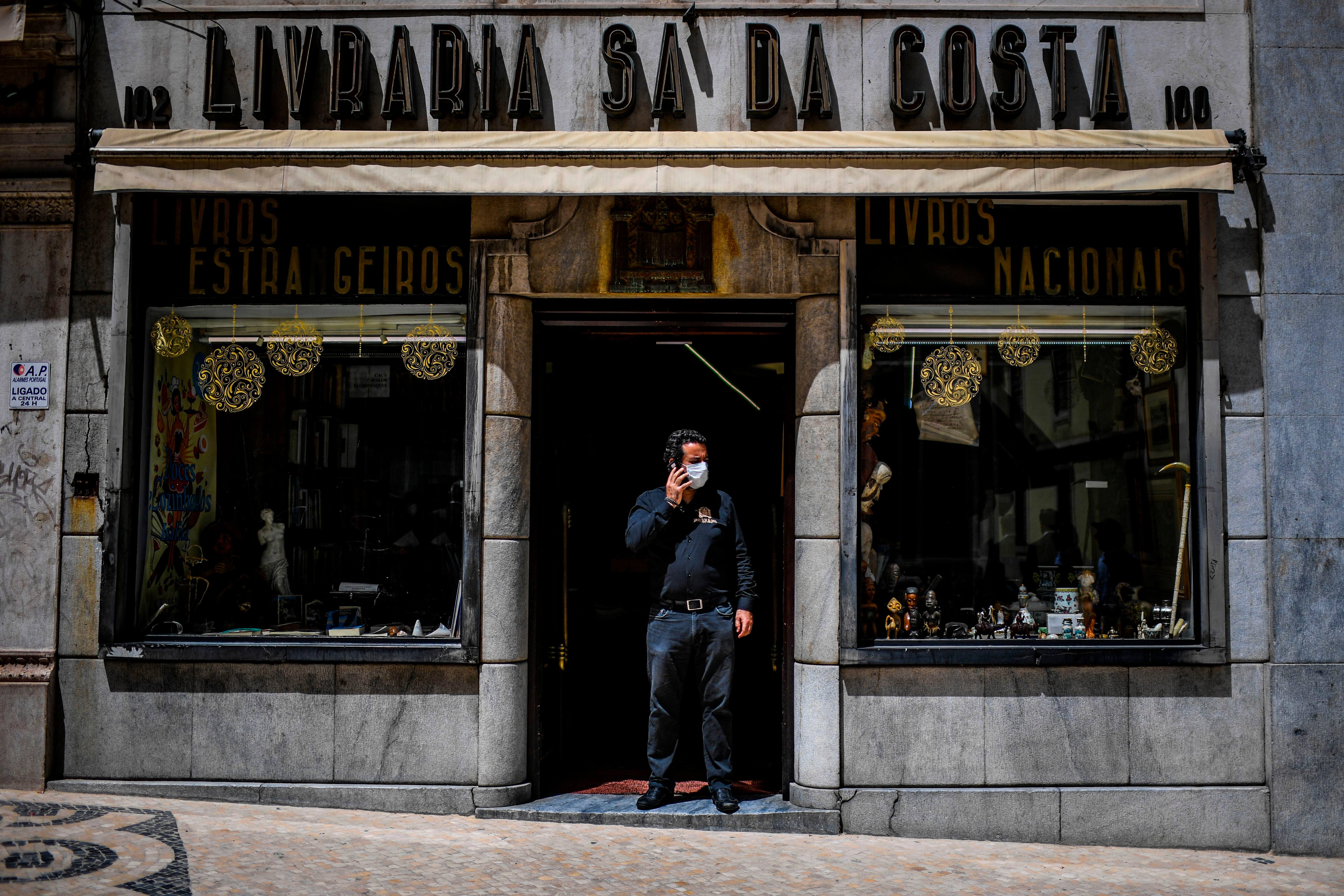 A man speaks on the phone in front of his bookshop in Lisbon on May 4, 2020 as millions of Europeans emerged with relief from coronavirus confinement. - Portugal allowed small shops, hair salons and car dealers to resume business, but ordered face masks to be worn in stores and on public transport. (Photo by PATRICIA DE MELO MOREIRA / AFP) (Photo by PATRICIA DE MELO MOREIRA/AFP via Getty Images)