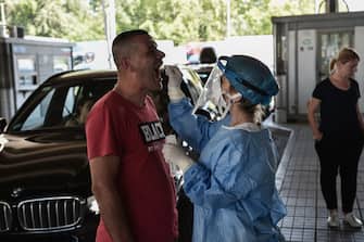 A public health worker collects a swab sample from a man to test for the COVID-19 coronavirus at the Greek-Bulgarian border crossing in Promachonas on June 19, 2020. - Thousands have already crossed the border with Bulgaria, the first overland checkpoint opened by Greek authorities on June 15 after the coronavirus lockdown in March to reach tourist destinations in northern Greece. (Photo by Sakis MITROLIDIS / AFP) (Photo by SAKIS MITROLIDIS/AFP via Getty Images)