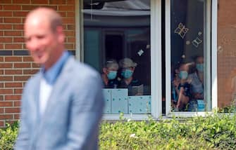 People wearing PPE (personal protective equipment), of a face mask or covering as a precautionary measure against spreading COVID-19, watch from a a window as Britain's Prince William, Duke of Cambridge talks to staff at Oxford Vaccine Group's facility at Churchill Hospital in Oxford, west of London on June 24, 2020, during a visit to learn more about the group's work to establish a viable vaccine against the novel coronavirus COVID-19. (Photo by Steve Parsons / POOL / AFP) (Photo by STEVE PARSONS/POOL/AFP via Getty Images)